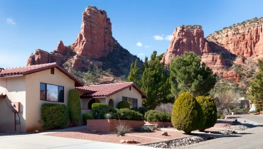 A desert-style home with a red tile roof, with towering red rock formations behind it.