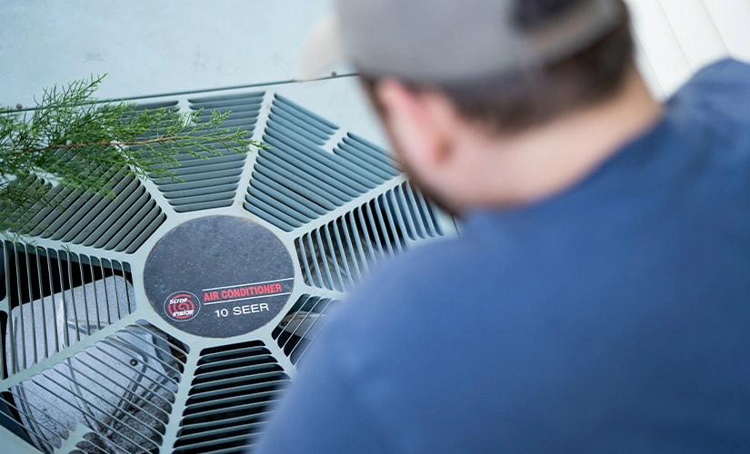 Overhead view of a man looking into the top of an air conditioning unit.