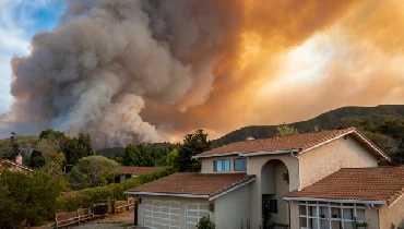 A residential home with large plumes of smoke visible in the background from raging wildfire fire.