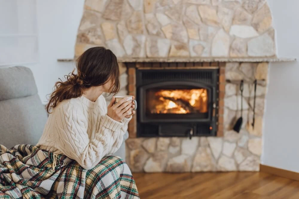 Young woman sitting home by fireplace.