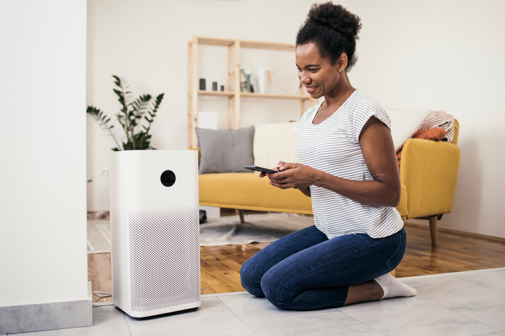 A woman sets up an air purifier with her mobile phone. | Aire Serv® of North Central Arizona