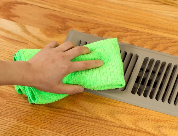 Close-up of floor vent being cleaned with bright green cloth.