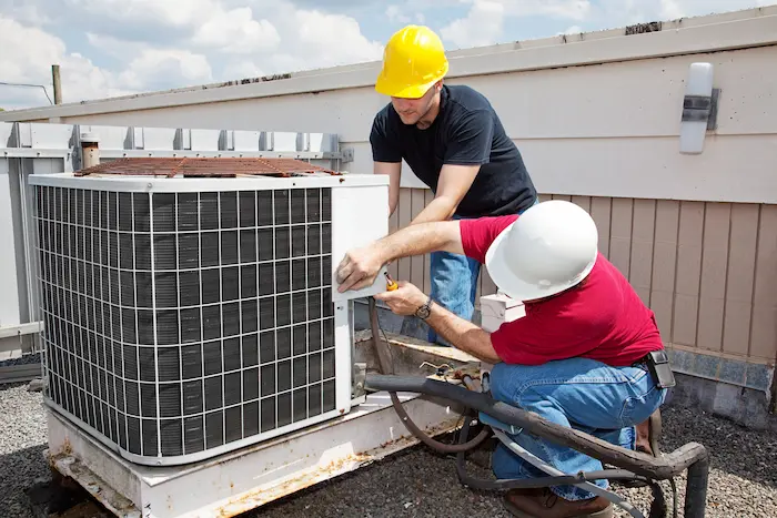 Pair of male technicians installing rooftop AC unit.