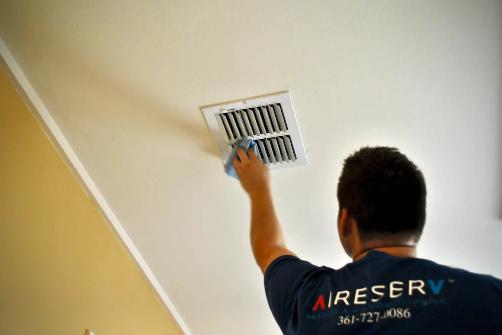 Male Aire Serv tech cleaning ceiling air vent.