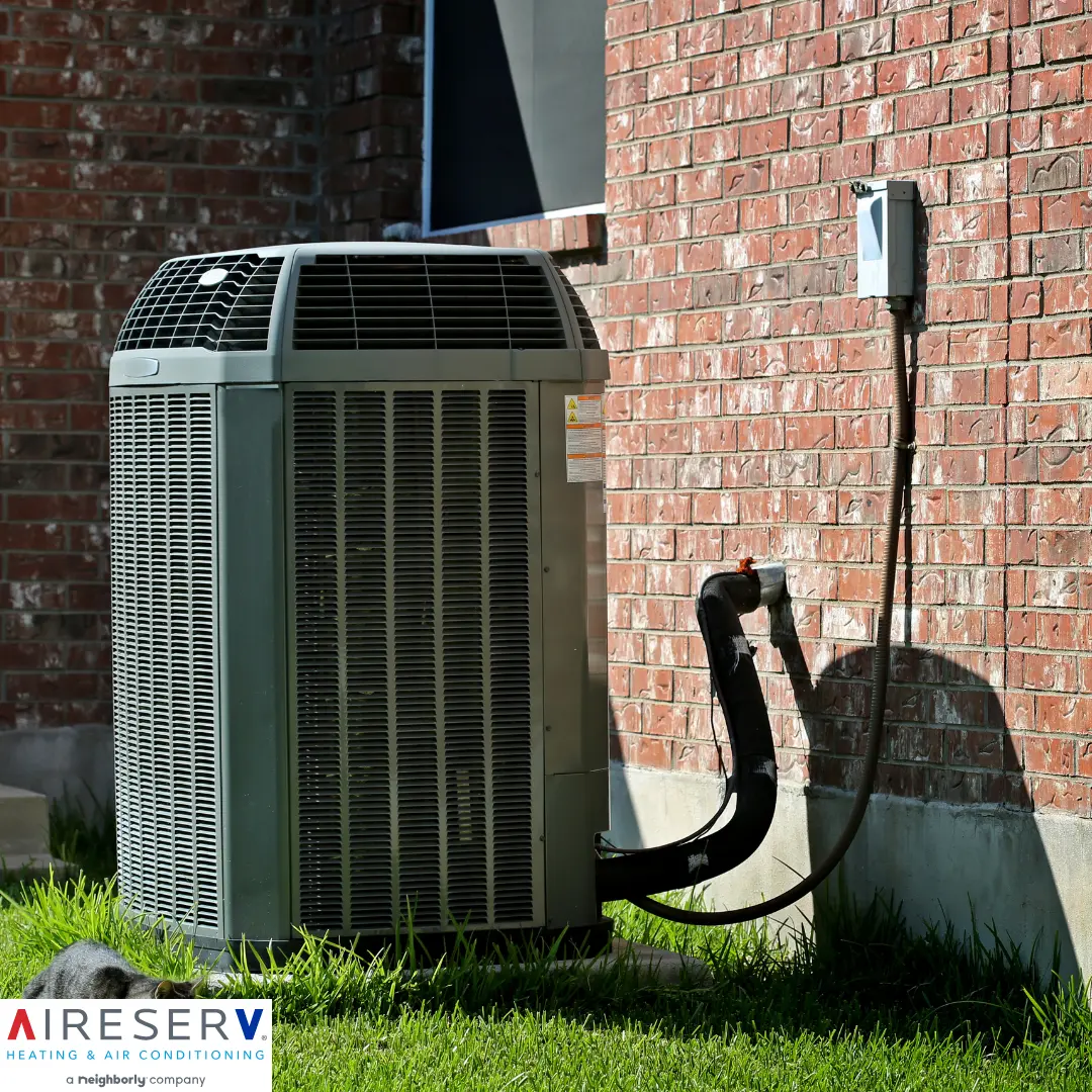 An outdoor air conditioning condenser unit installed beside a brick wall, with visible refrigerant lines and an electrical connection box.