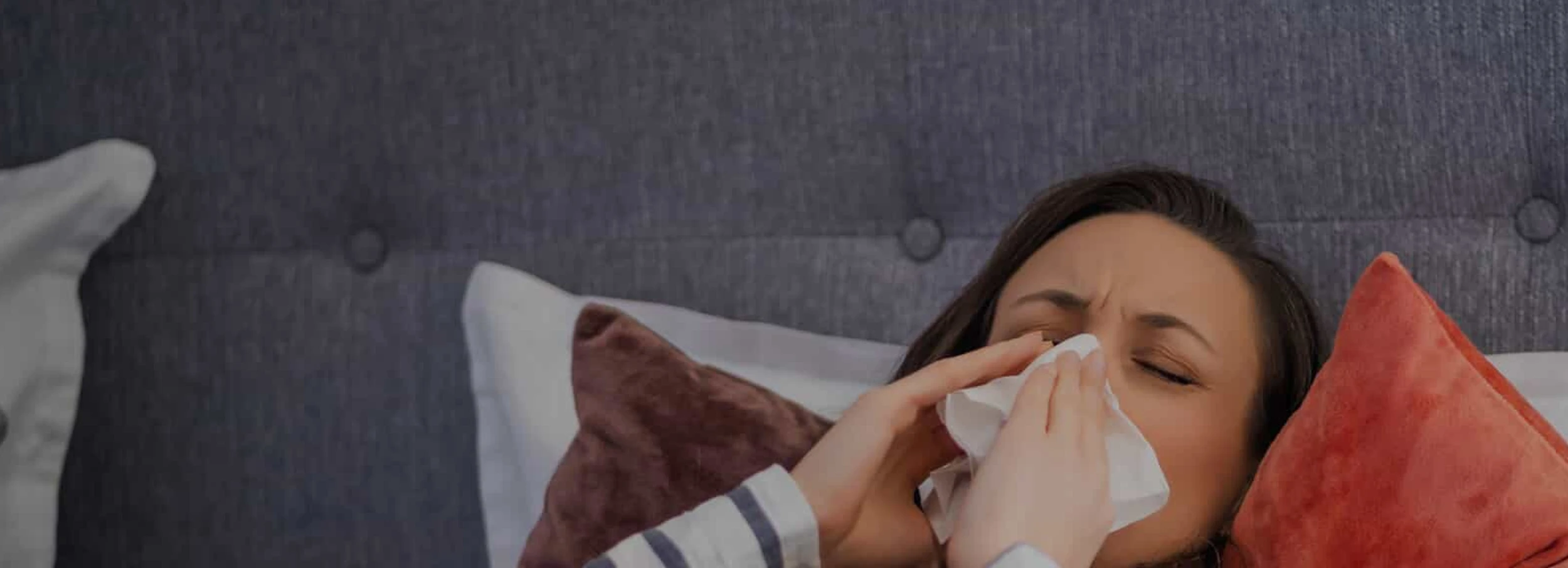 woman laying in bed sneezing into a kleenex.