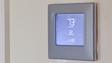 Silver non-programmable thermostat displaying seventy-three degrees Fahrenheit onscreen.