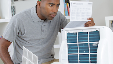 African American man in gray polo shirt inspecting paper with instructions beside HEPA air filter.