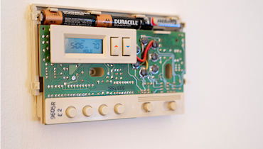 Non-programmable digital thermostat with cover removed exposing batteries and circuit board.