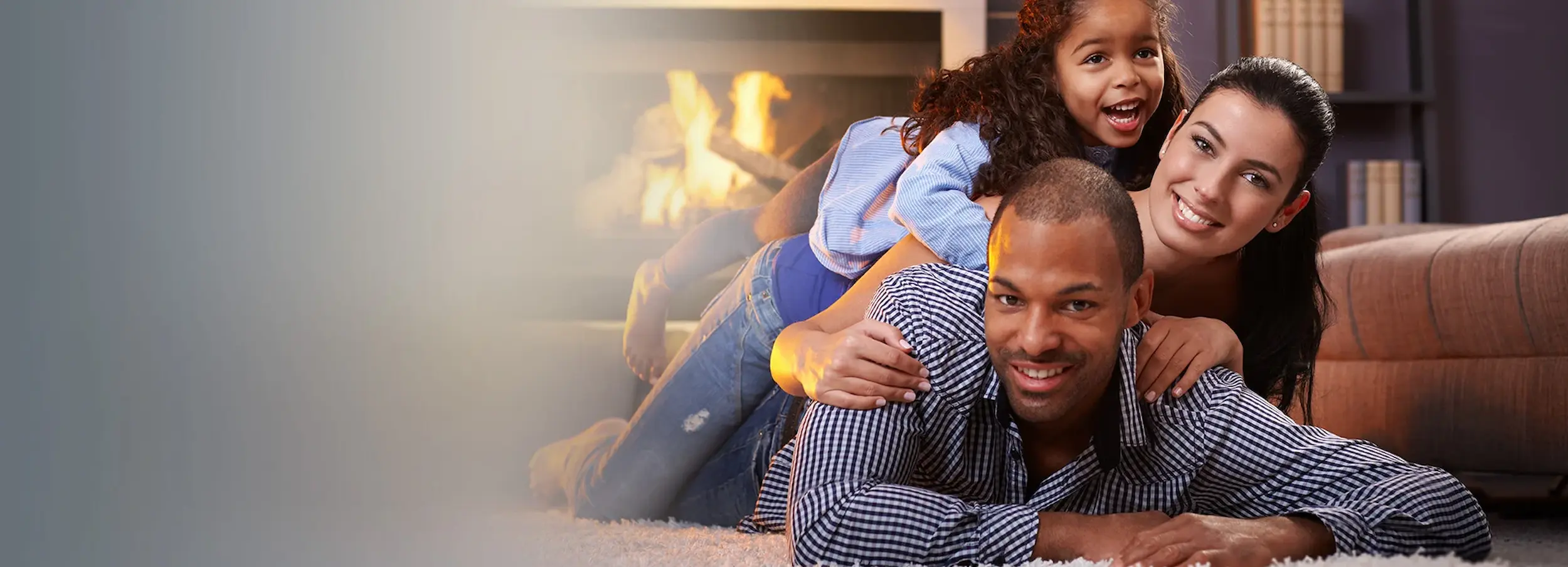Smiling African American couple with child lying piled on a rug in a living room in front of a fireplace.