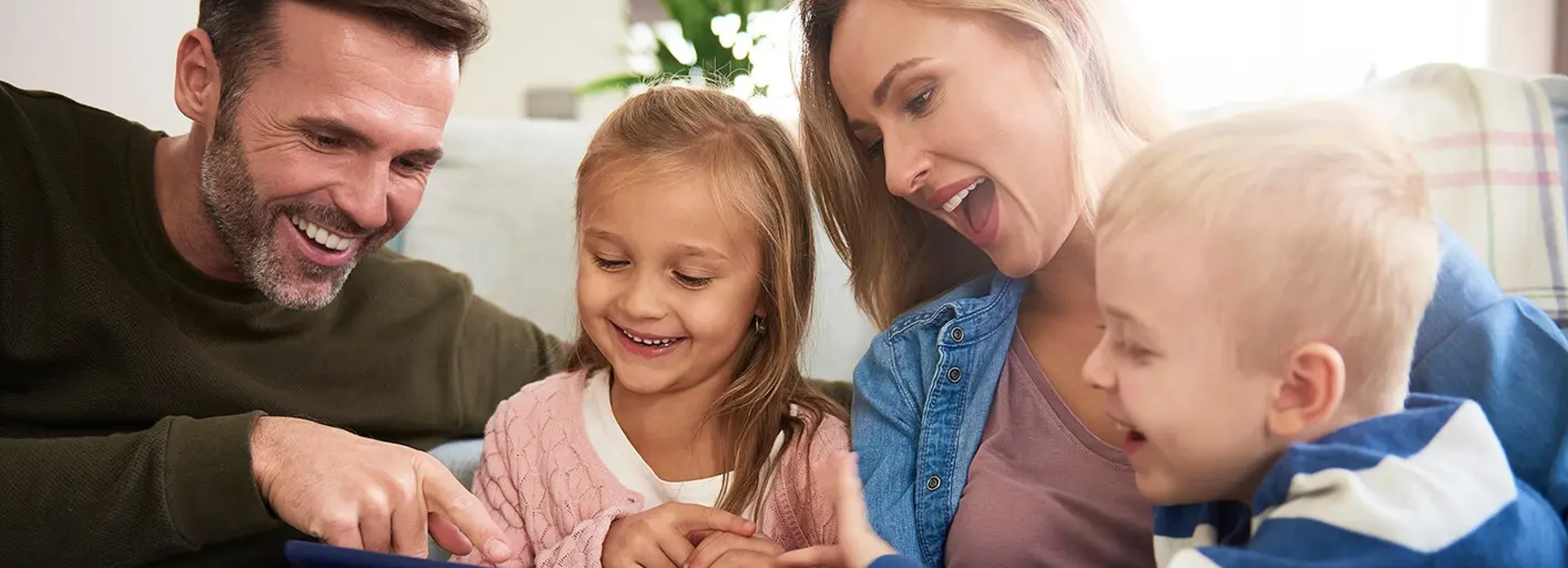 Happy family of four laughing at something on a tablet.