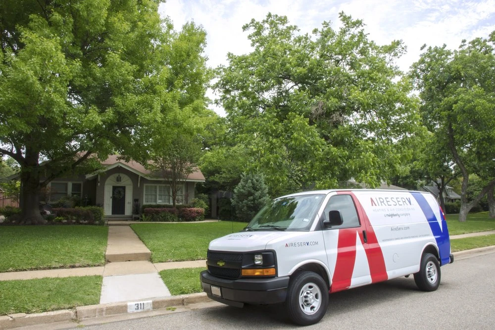 An HVAC work van with the Aire Serv logo parked outside of a home where heater replacement is being performed.