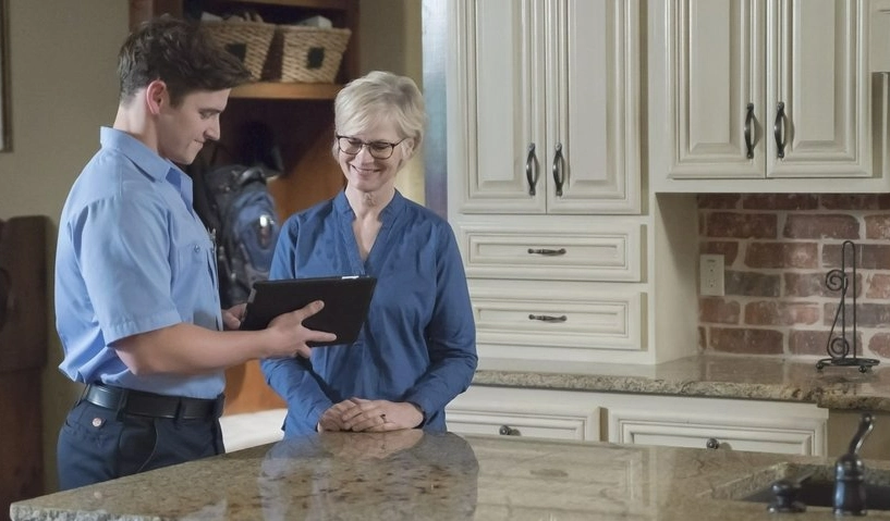 An HVAC service professional from Aire Serv pointing out a detail about heating to a homeowner on the screen of their thermostat.