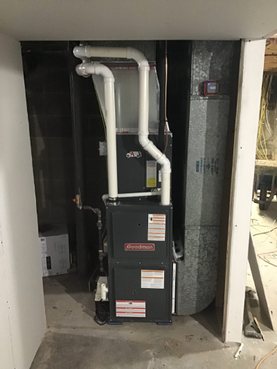 A newly installed Goodman furnace in a small space behind a wall inside of a home where furnace replacement has been completed by Aire Serv.