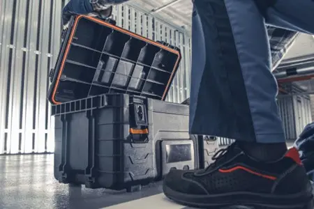 A large black plastic toolbox open on the floor of a commercial facility, with a technician's leg visible next to it