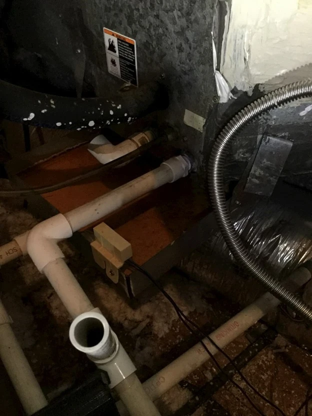 The back of a furnace in Irving, TX being repaired by Aire Serv, with visible pipes and other connections for fuel and the furnace’s exhaust.