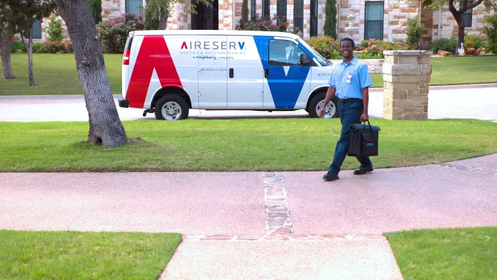 An Aire Serv HVAC repair professional walking from a work van to a home in need of heater repair in Dallas, TX.